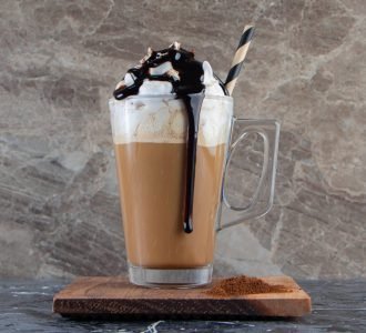 Glass of foamy cold coffee with whipped cream and chocolate on wooden plate. High quality photo